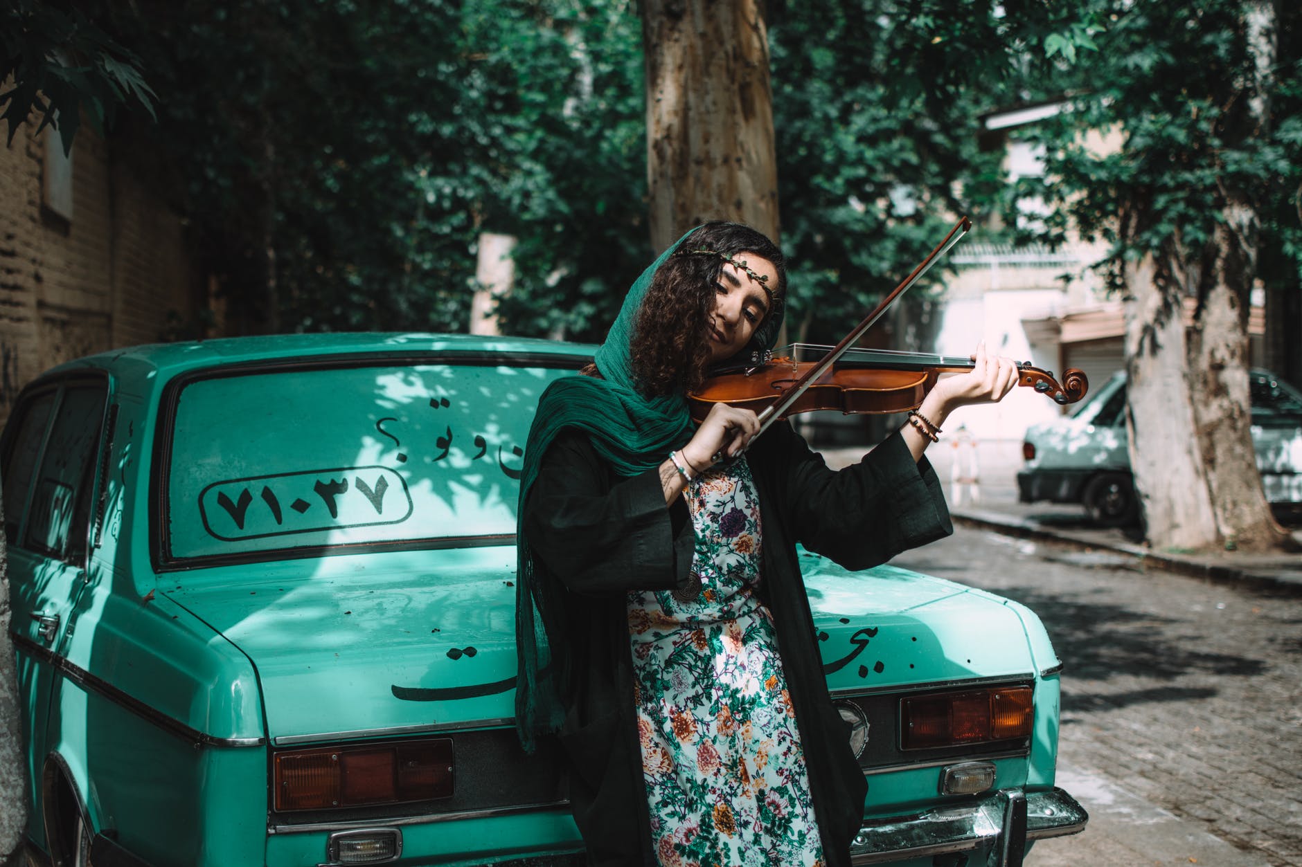 woman playing violin while leaning on green vehicle