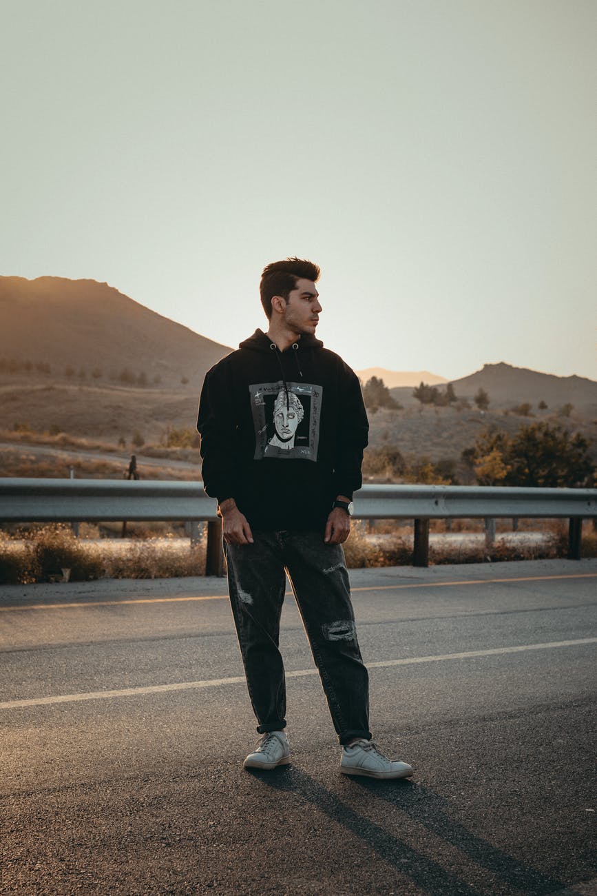 man in black and white sweater standing on road