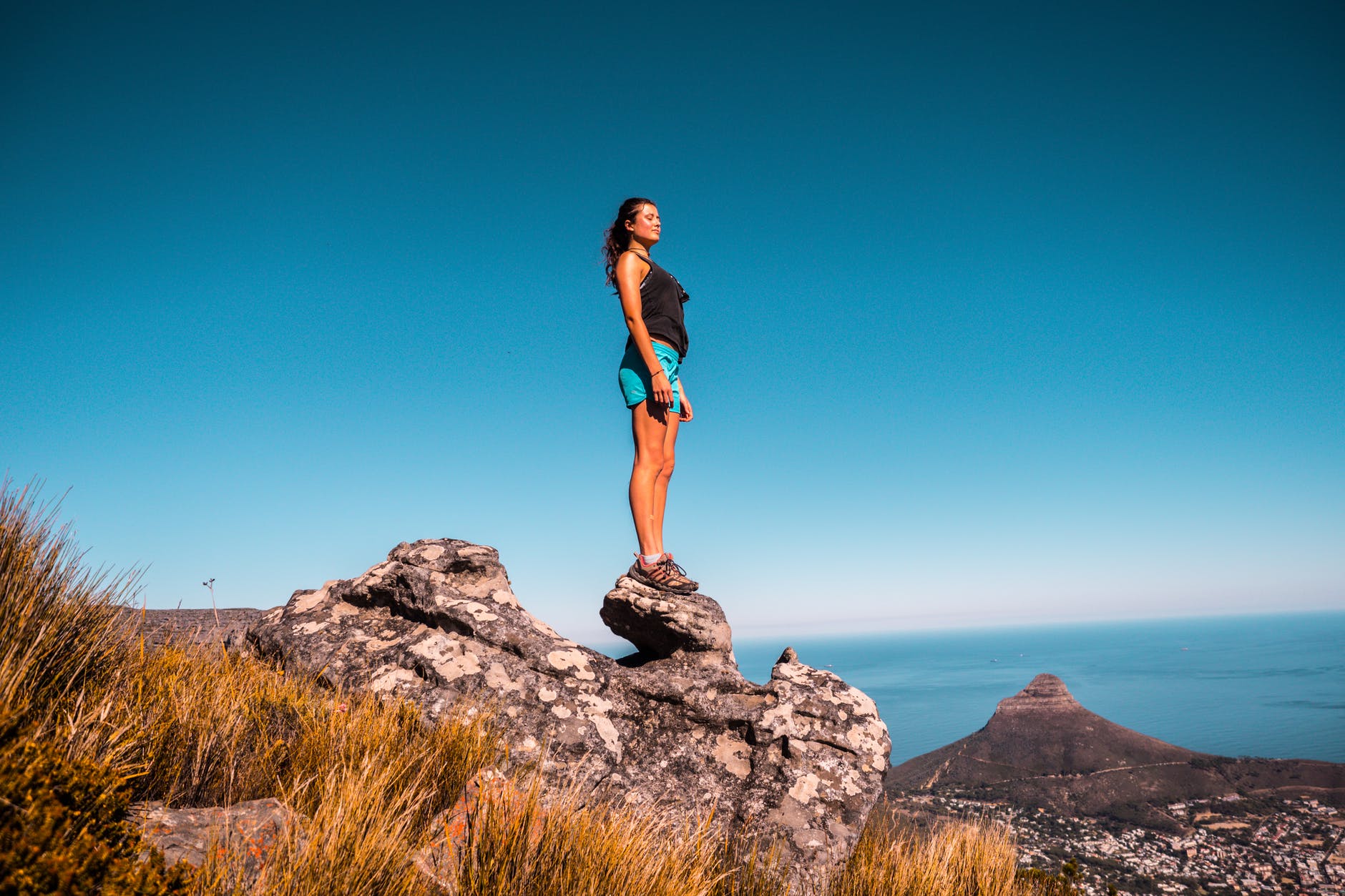 woman in black top and blue shorts on stone under blue sky